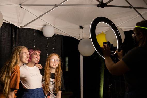三名学生在环形灯光前摆姿势拍照，背景是气球